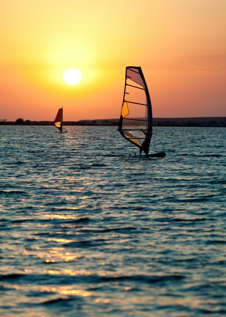Still sea surface, man practicing wind surfing and golden sunset in sky
